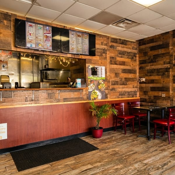 Cozy restaurant interior featuring wooden walls, a service counter, menu boards, and red dining chairs.